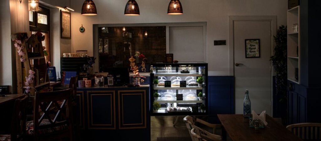 Best Place to Eat in Dalhosuie - The cozy interior of Cafe Refred located in Dalhousie, Himachal Pradesh, featuring warm pendant lighting, a pastry display case, and wooden seating.