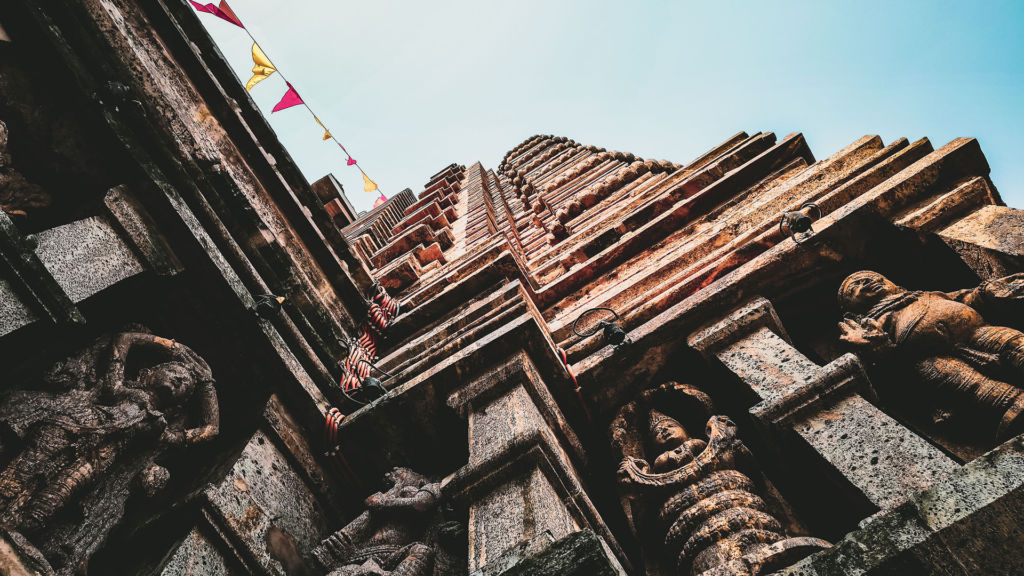 Carved temple spire viewed from below with prayer flags against the sky