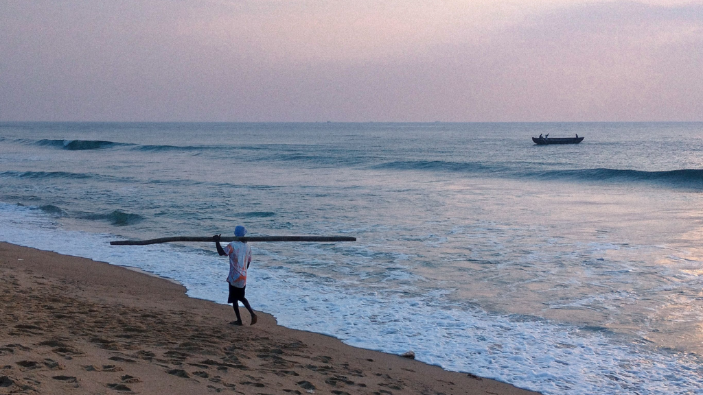Fisherman walking along Golden Beach at dusk with a boat offshore | Best Things to Do in Puri