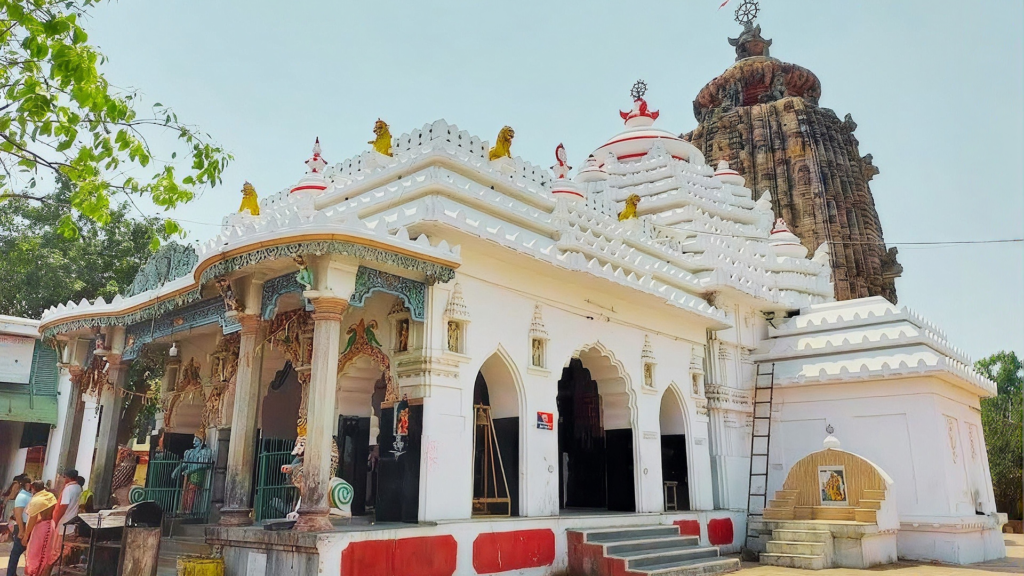 A white temple structure with the Jagannath Temple tower rising behind it, a smaller shrine within the temple complex