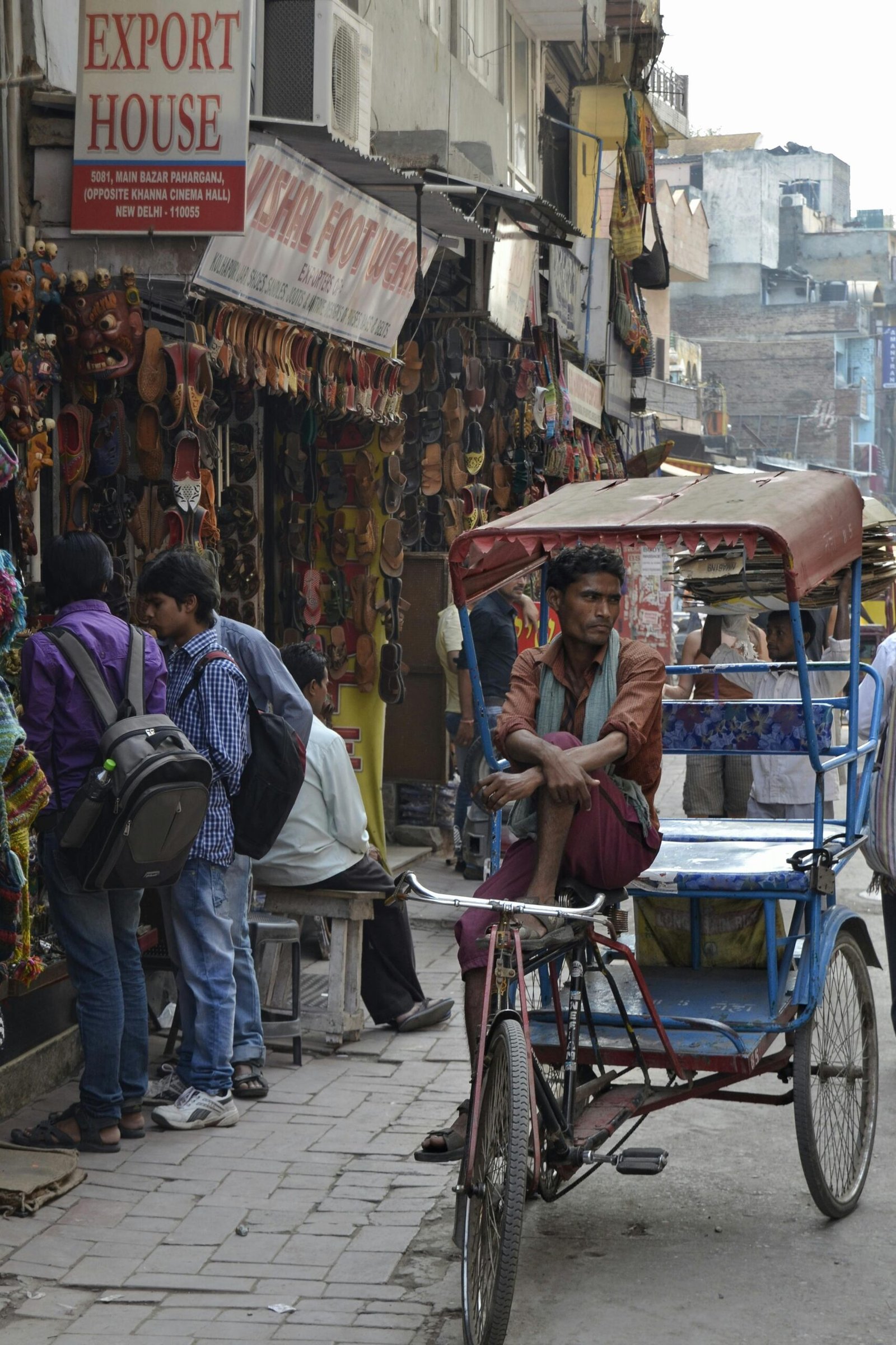 A busy street scene in Old Delhi with a cycle rickshaw driver and local market shops selling traditional goods.