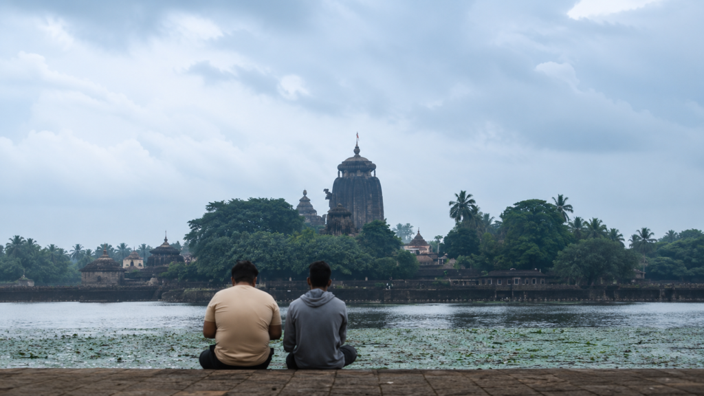 Things to Do in Bhubaneswar: A Complete Guide 4 Two travellers sitting by Bindu Sagar Lake facing the Lingaraj Temple complex | Things to Do in Bhubaneswar