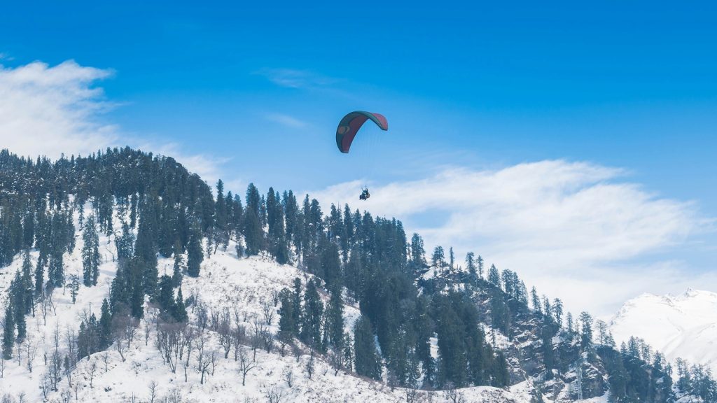 Paraglider flying above snow-covered pine slopes in Solang Valley near Manali